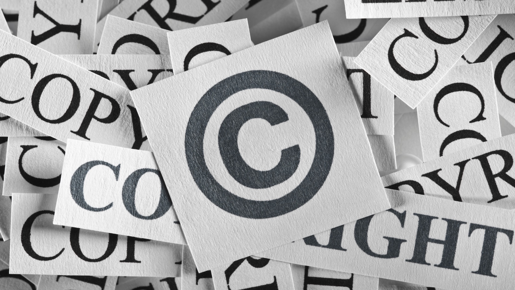 Close-up of paper cards printed with the copyright symbol, surrounded by scattered cut-out letters spelling “copyright.”