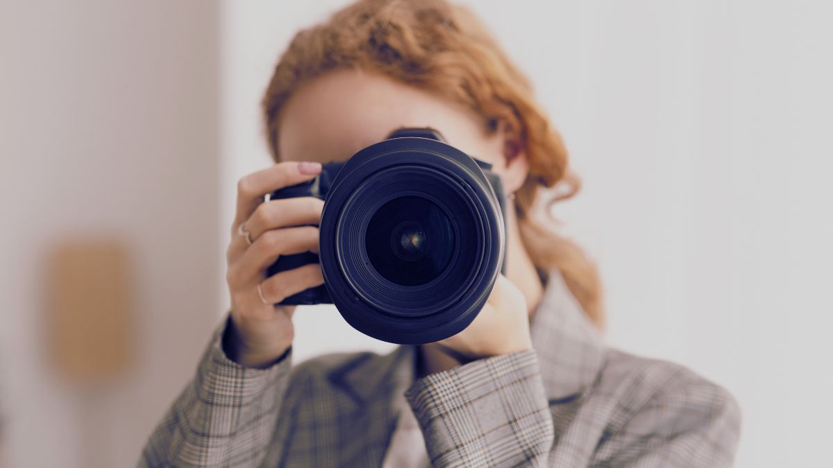Person holds a camera up to their face, taking a photo indoors, with the camera lens in sharp focus.